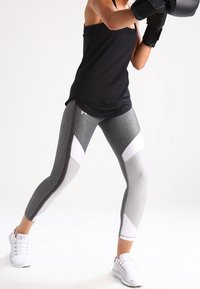 Leggings atletici grigi con pannelli geometrici bianchi e neri, abbinati a una canotta nera e a guantoni da boxe, indossati con scarpe sportive bianche.