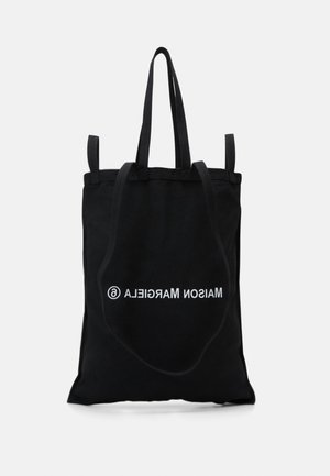 Sort shopper-taske med lange håndtag, der har hvide omvendte bogstaver "MAISON MARGIELA" og et cirklet "a" logo midt på fronten.