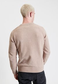 Jasnoróżowy sweter z dzianiny o fakturowym wykończeniu, okrągłym dekolcie oraz ściągaczach na rękawach i u dołu. Widok z tyłu; noszony z ciemnymi spodniami.