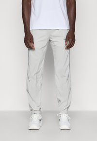 Lichtgrijze sportbroek met een taps toelopende pasvorm, zachte textuur, elastische boorden, zijzakken en subtiele contrasterende stiksel-details.