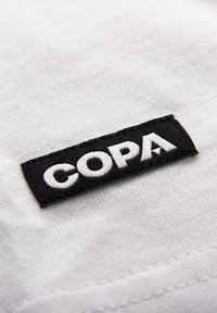 Black fabric label with white bold letters "COPA" stitched onto textured white cloth.