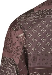 Chemise à manches longues arborant des motifs cachemire et géométriques dans des tons de brun, avec une texture lisse et soyeuse et des détails contrastants.
