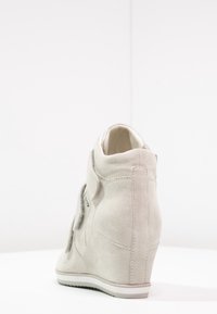 Szary zamszowy sneakers na koturnie o gładkiej fakturze, z zaokrąglonym noskiem i dyskretną białą gumową podeszwą. Widok z tyłu podkreśla konstrukcję i szwy.