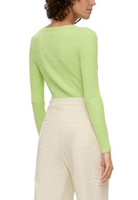 Pull en maille côtelée vert clair avec des manches longues, un décolleté large, associé à un pantalon cargo taille haute blanc cassé avec poches arrière.