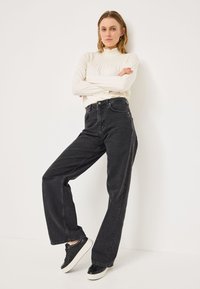 Črne široke jeans hlače z visokim pasom in petimi žepi, v kombinaciji s kremo dolgimi rokavi majico s smock teksturo in volančki okoli vratu.