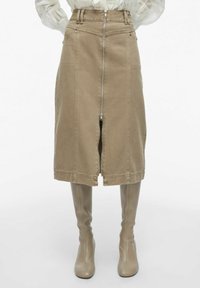Falda de mezclilla caqui con cremallera frontal, diseño estructurado, costuras visibles y corte a la altura de la rodilla, combinada con botas altas a juego.