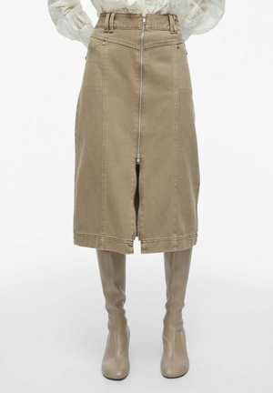 Falda de mezclilla caqui con cremallera frontal, diseño estructurado, costuras visibles y corte a la altura de la rodilla, combinada con botas altas a juego.