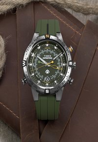 Timex Expedition Uhr mit grünem Gummiband und schwarzem Edelstahlgehäuse. Verfügt über ein dunkelgrünes Zifferblatt, Kompassmarkierungen und gelbe Akzente.