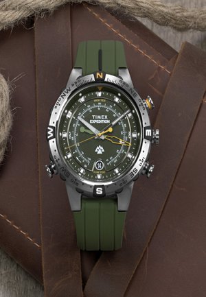 Reloj Timex Expedition con correa de goma verde y caja de acero inoxidable negro. Presenta una esfera de color verde oscuro, marcas de brújula y acentos amarillos.