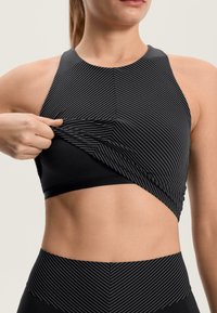 Čierny atletický crop top s bielymi vertikálnymi pruhmi, s priliehavým strihom a vrstveným efektom. Materiál pôsobí hladko a elasticky.