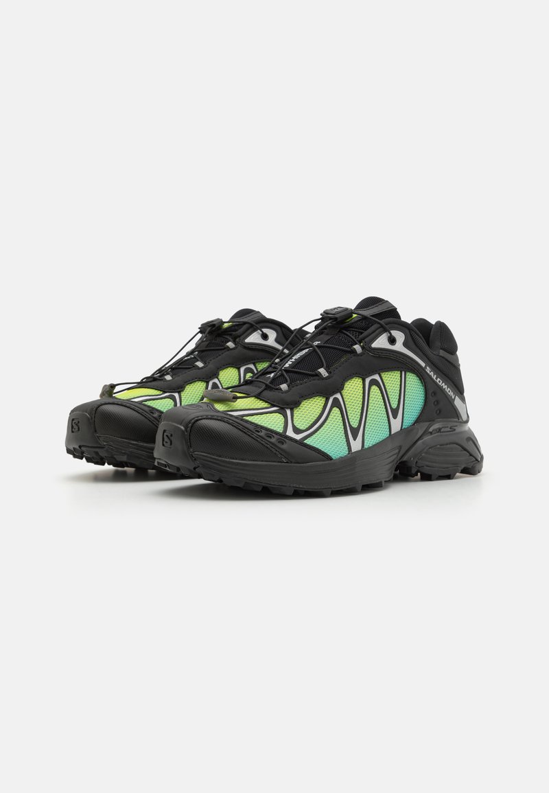 Zapatillas deportivas negras con paneles de malla verde y azul, una suela de goma texturizada y un sistema de cordones rápido para un ajuste ajustable.