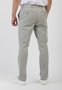 Pantaloni di cotone grigio chiaro con vestibilità slim, dotati di due tasche posteriori con chiusura a bottone e dettagli di cucitura discreti sui lati.