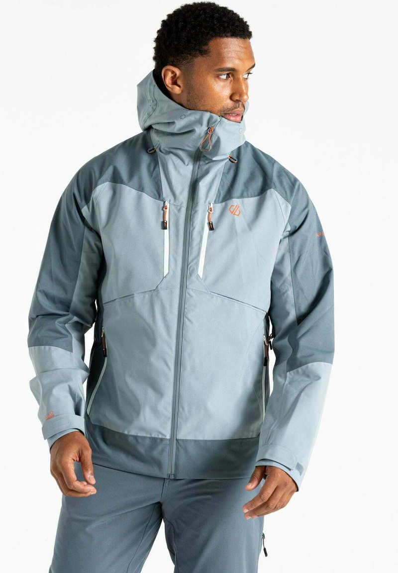 Veste imperméable bleu clair avec un col haut, des poches zippées et des sections contrastantes de bleu plus foncé. Équipée de poignets ajustables et de cordons de serrage.