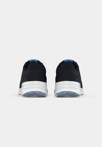 Paire de chaussures de sport noires avec semelles blanches vues de dos, montrant un tissu en mesh et des accents bleus sur un fond uni.