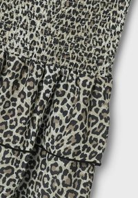 Mit einem gepufften Oberteil in einem Leopardenmuster in Beige und Schwarz, mit einem rüschenbesatz. Der Stoff wirkt leicht und hat eine strukturierte Oberfläche.