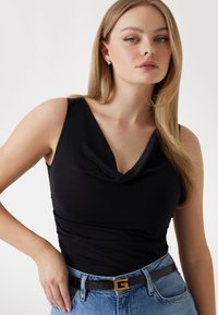 Top nero senza maniche con design a collo a giogo, realizzato in un tessuto liscio. Indossato con jeans in denim a vita alta e una cintura con fibbia dorata.