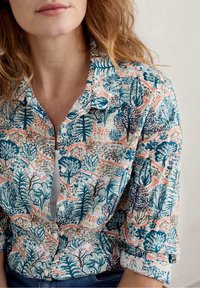 Kurzärmelige Bluse mit einem bunten botanischen Druck in Blau, Grün und Koralle, mit einem Knopfkragen und einer weichen Textur.