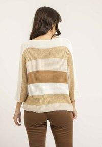 Pull en tricot de couleur beige, crème et rayures marron clair. Manches trois-quarts, coupe ample, motif texturé. Associé à un pantalon marron.