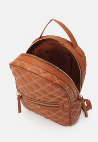 Mochila de cuero marrón acolchada con cremallera dorada, que cuenta con un asa y un bolsillo frontal. Interior forrado con una tela a juego, incluye compartimentos.