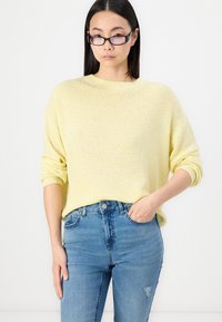 Yellow knit sweater with a relaxed fit and rolled sleeves, paired with light blue high-waisted jeans featuring a distressed detail.