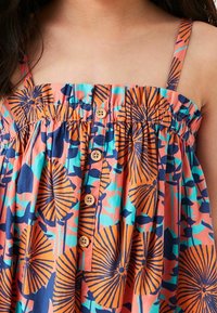 Gros plan d'une robe sans manches avec un motif floral orange, bleu et turquoise et des boutons en bois sur le devant.