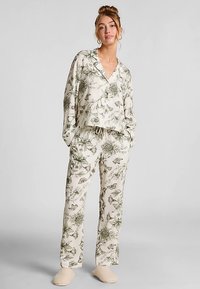 Loungewear-set met bloemenpatroon in off-white met groene botanische ontwerpen; bestaat uit een top met V-hals en broek met elastische tailleband. Zachte stof.