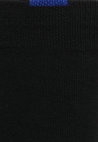 Schwarze Socke mit geripptem Design und blauer Bündchen. Das Material wirkt dehnbar mit einer glatten Oberfläche. Das Design ist schlicht und funktional.