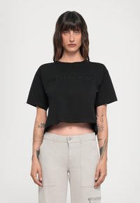 Juodas trumpas marškinėlis su trumpomis rankovėmis, turintis iškilų "MICHAEL KORS" logotipą. Minkšta medvilnės medžiaga, laisvas kirpimas, be raštų ar metalinių detalių.