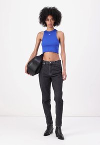 Modrý žebrovaný crop top, černé džíny s vysokým pasem a černé kotníkové boty. Drží zakřivenou černou kabelku. Jednoduchý, přiléhavý design.