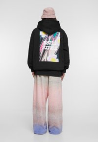 Juodas džemperis su spalvotu grafiniu piešiniu "RETRO FUTURE" nugarinėje pusėje. Derinamas su plačiomis, gradientinėmis kelnėmis, turinčiomis rožinės ir mėlynos spalvų atspalvius, pasižyminčiomis minkšta tekstūra.