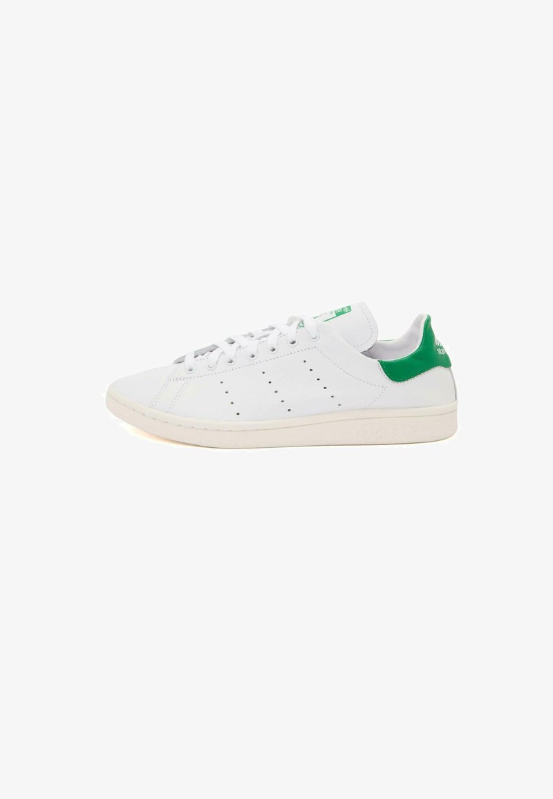 Zapatilla de cuero blanca con acentos verdes en el talón y la lengüeta. Presenta un diseño perforado en los lados y una suela de goma texturizada.