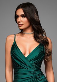 Grön satindress med djup V-ringning, rynkad struktur och tunna axelband. Bärs med ett glittrande choker-halsband. Bakgrunden är neutral grå.