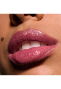 Kolor ust w delikatnym mauve z połyskującym wykończeniem. Pełne usta z wyraźnymi konturami, podkreślające gładką teksturę w zestawieniu z karnacją.