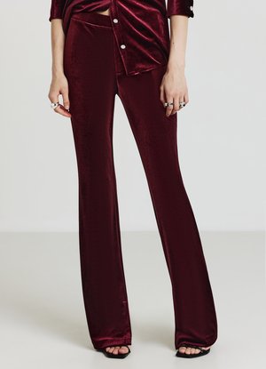 Pantaloni svasati in velluto color bordeaux con una texture liscia e vita aderente. L'orlo presenta un design a ritaglio, abbinato a una maglia coordinata.