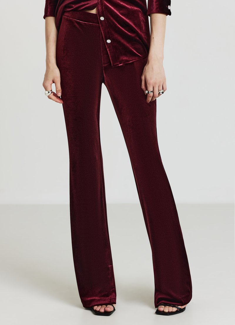 Pantaloni svasati in velluto color bordeaux con una texture liscia e vita aderente. L'orlo presenta un design a ritaglio, abbinato a una maglia coordinata.