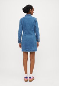 Denim obleka s ovratnikom, dolgimi rokavi in prilegajočim krojem. Ima zadnji šiv in rahlo robno podrobnost. Nosimo jo z barvitimi platform čevlji.