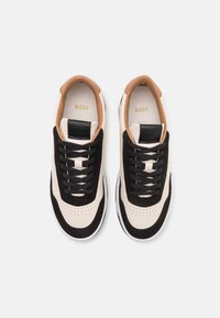 Paire de baskets basses crème et noires avec doublure intérieure beige, lacets noirs, zone des orteils perforée et logo "BOSS" sur la languette et la semelle intérieure.