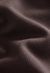 Tissu brun foncé texturé avec un petit motif en grille en relief, délicatement plié pour montrer la profondeur et les ombres.
