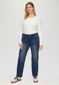 Blauwe high-waisted straight-leg jeans met vijf zakken en een sluiting met een knoop aan de voorkant, gecombineerd met een witte lange mouwen shirt en casual sneakers.
