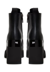 Botas de cuero negras hasta el tobillo con un tacón cuadrado negro brillante, cierre de cremallera y textura suave. Presentan una punta redondeada y líneas limpias.