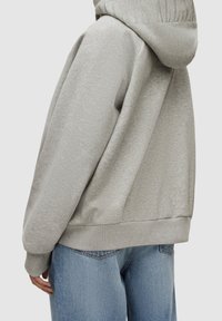 Felpa grigia con cappuccio in tessuto morbido con vestibilità rilassata. Presenta polsini e orlo a coste, con un sottile marchio sul retro del cappuccio.