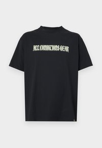 Čierne bavlnené tričko s krátkymi rukávmi, ktoré má na prsiach nápis "ALL CONDITIONS GEAR" v zelenom štýlovom písme. Priame strih.