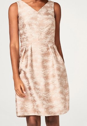 Mouwloze beige jurk met abstract patroon, V-hals, getailleerde taille en geplooide rok gedragen door een staand persoon.