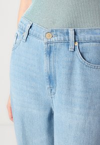 Des jeans en denim bleu clair présentent un design taille haute, des poches avant, une fermeture à bouton et une finition texturée subtile.