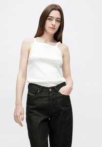 Biely rebrovaný tielkový top s úzkymi ramienkami, v kombinácii s tmavými džínami s vysokým pásom, ktoré majú predné vrecká a ozdobné kontrastné švy.