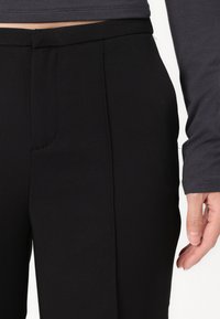 Μαύρο τακτοποιημένο παντελόνι με απαλό ύφασμα, διαθέτει επίπεδο μπροστινό μέρος και πλαϊνές τσέπες, σε συνδυασμό με γκρι μπλούζα με μακρύ μανίκι.