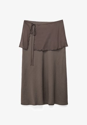 Pruun midipikkusega seelik läbipaistva rätikukujulise ülekattega, mis on vasakul küljel lipsuks seotud, ja millel on peen tekstuuriga kangas.