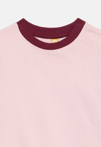 Lys rosa sweatshirt med ribbestrikket burgunder rund hals. Glatt tekstur, lange ermer og et enkelt, klassisk design uten mønstre eller aksenter.