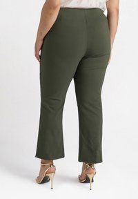 Tmavě zelené, slim fit kalhoty s rozšířeným spodním lemem, vyrobené z hladké látky. Mají vysoký pas a detail výstřihu na lemu.