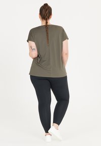 Olivgrön kortärmad topp med en avslappnad passform, sydd söm ner längs ryggen, tillsammans med svarta leggings och vita sneakers.